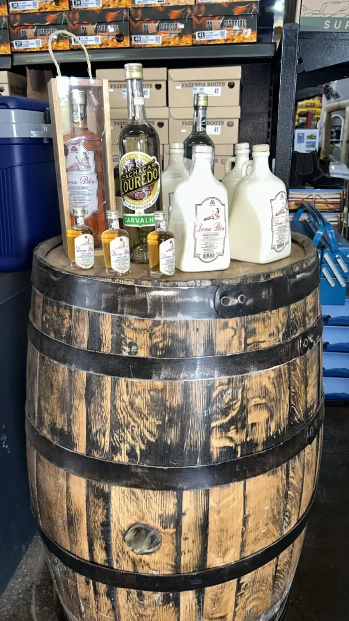 Cachaça artesanal em cima de um barril de carvalho, com caixas de botina ao fundo